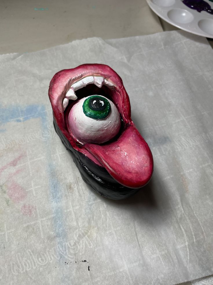 an odd looking object with green eyes on top of a piece of white wax paper