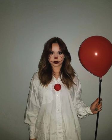 a woman in white shirt and clown makeup holding a red balloon with one eye open