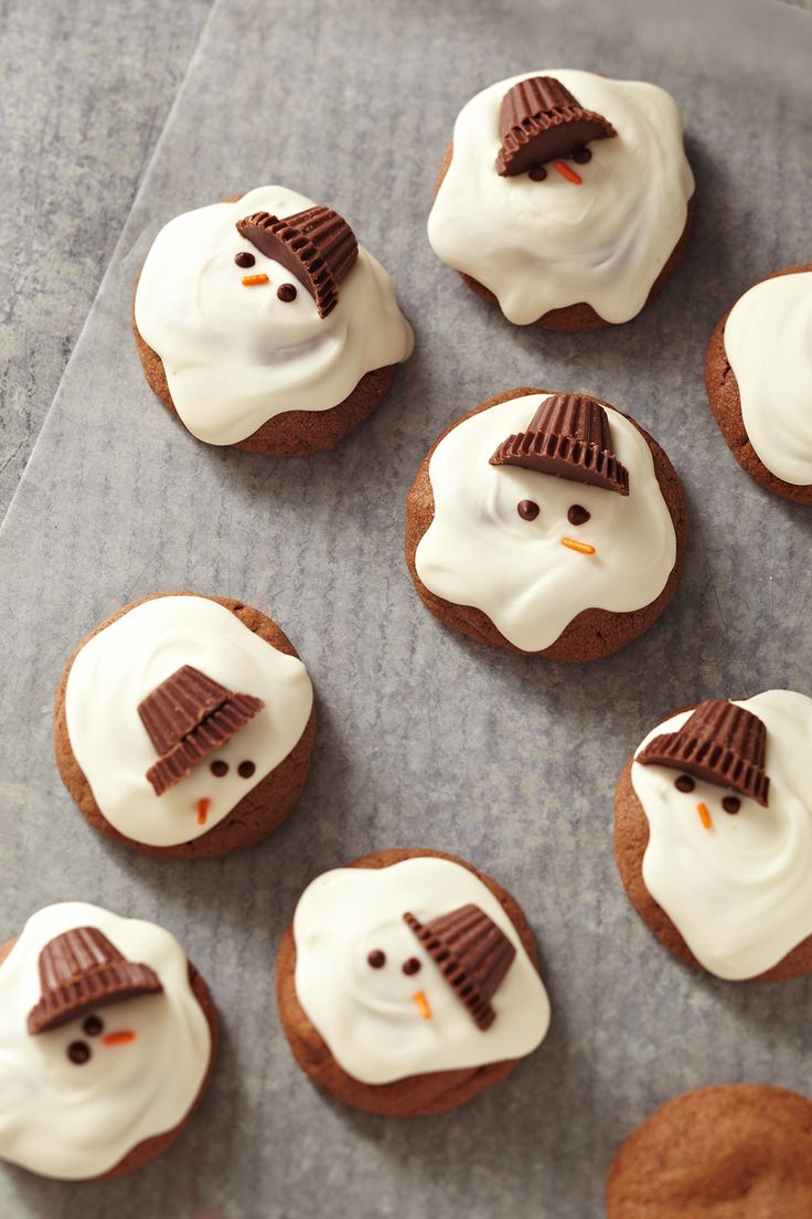 frosted cookies decorated like snowmen with chocolate hats on their heads and noses, sitting on a baking sheet