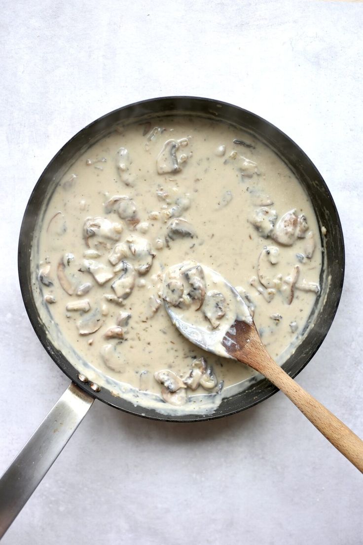 a pan filled with mushrooms and sauce on top of a white countertop next to a wooden spatula