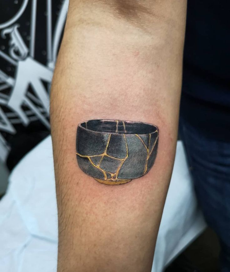 a black and gold bowl tattoo on the arm