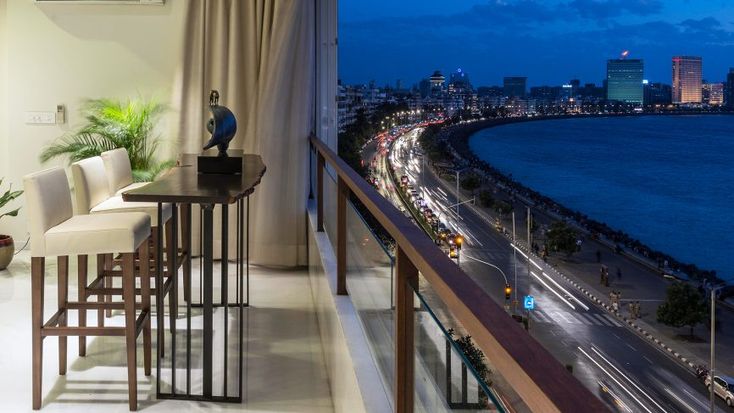 a dining table and chairs on a balcony overlooking the ocean at night with city lights in the distance