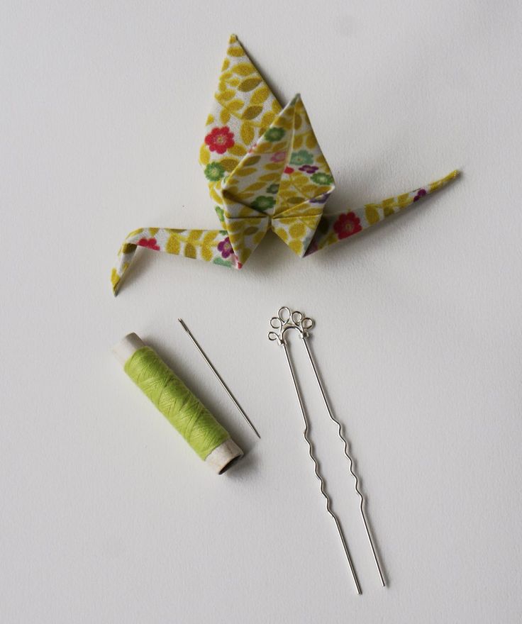 an origami bird next to sewing needles and thread