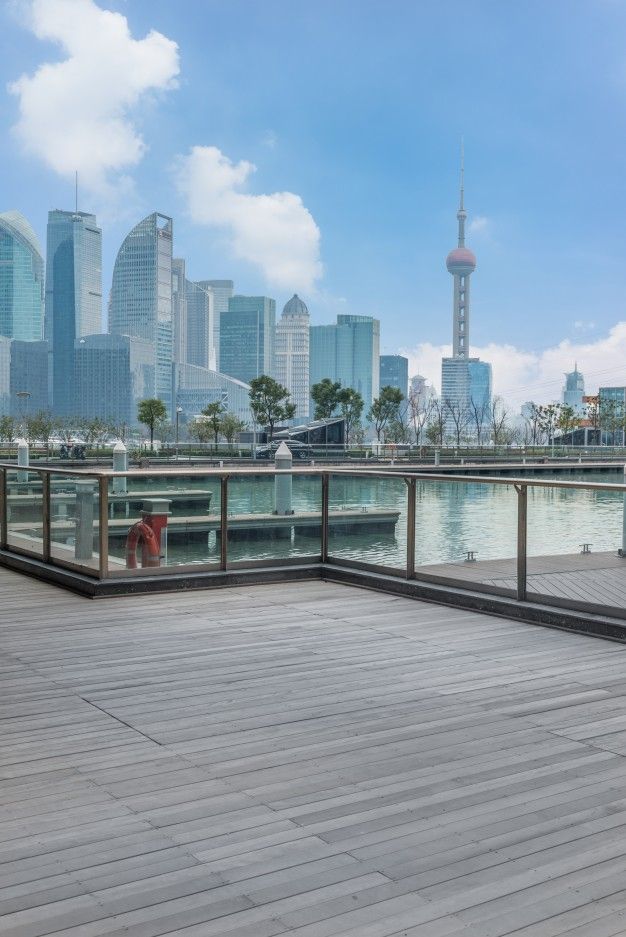 an empty wooden deck overlooking a cityscape with water and buildings in the background