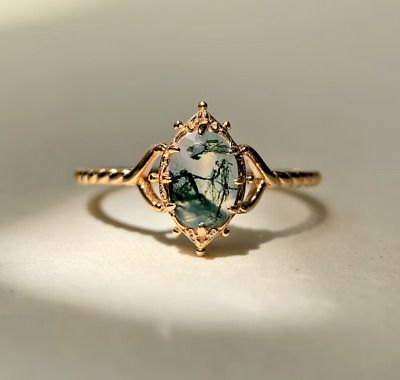 a gold ring with a green and white stone in the center on a white surface