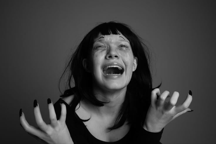 a woman with black and white makeup holding her hands in front of her face as if screaming