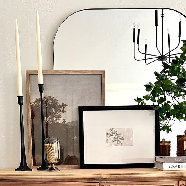 a dresser with candles and pictures on it, next to a plant in a vase