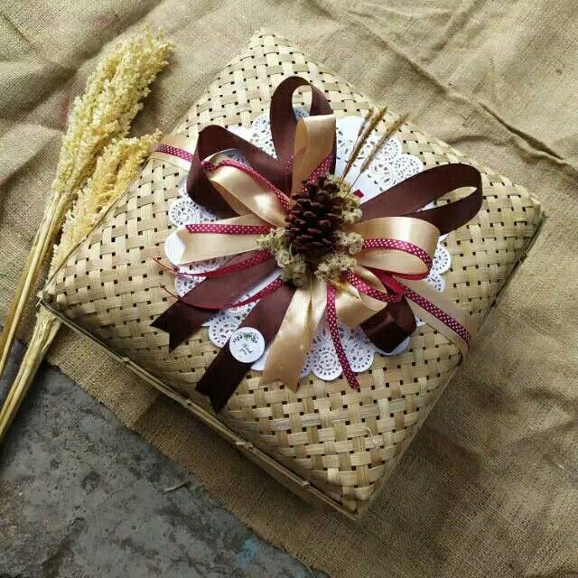 a gift wrapped in brown ribbon with a decorative flower on the top and two straw stalks next to it