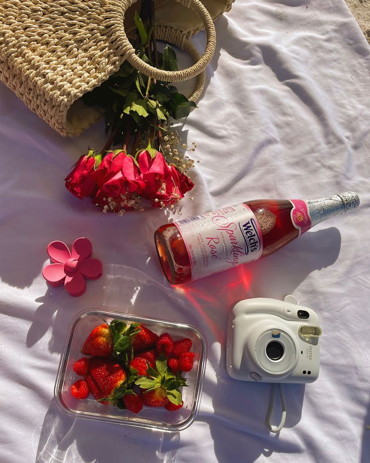 strawberries, flowers and a camera on a white table cloth next to a wicker basket