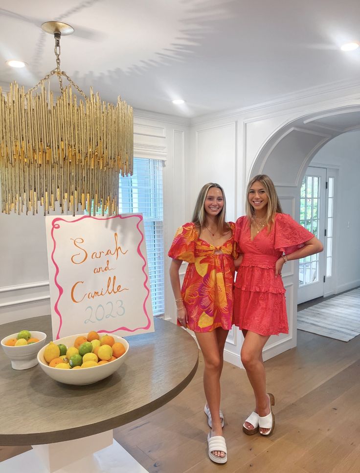 two women standing in front of a table with fruit on it