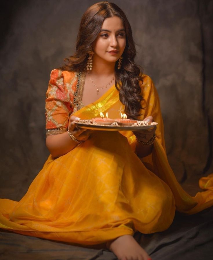 a woman sitting on the ground holding a cake with lit candles in her hand and looking at the camera