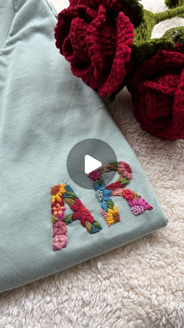 an embroidered t - shirt with the letter m on it next to some crocheted flowers