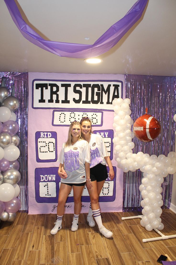 two girls standing in front of a football themed backdrop with balloons and streamers on the wall