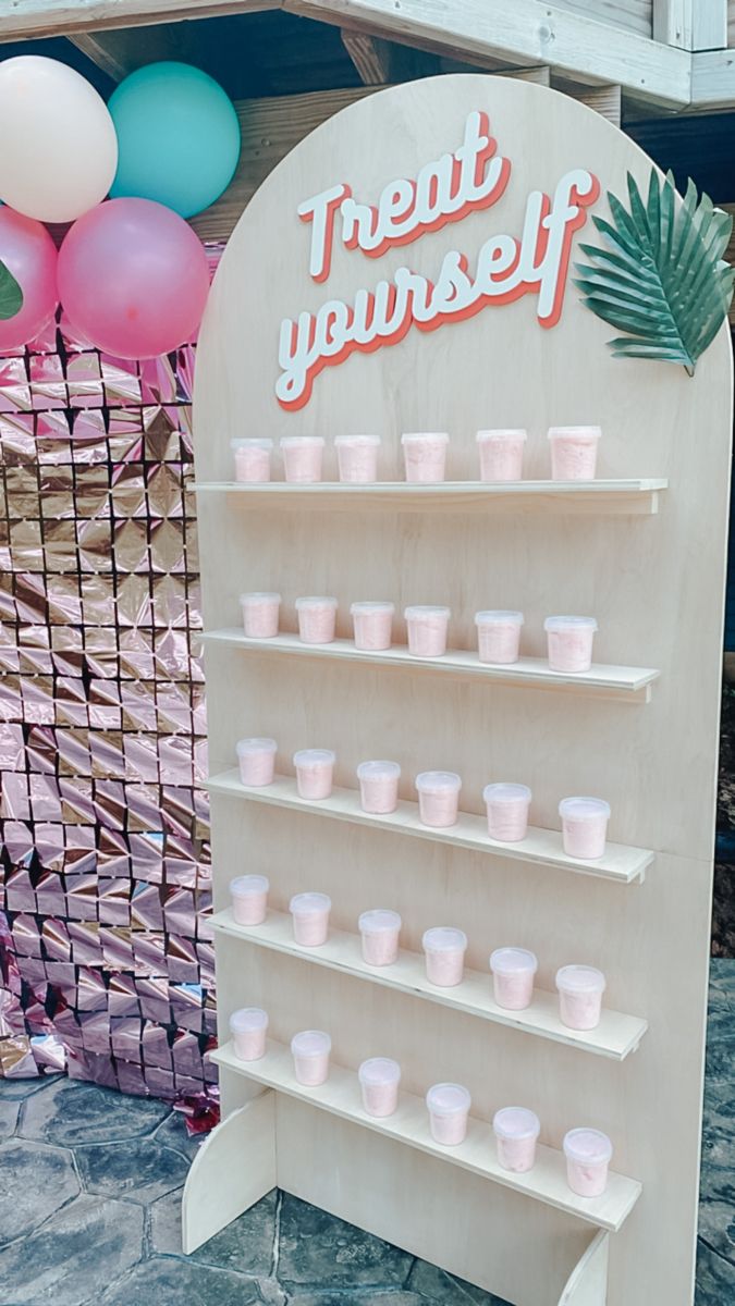 there is a sign that says treat yourself with cups on the shelf and balloons in the background