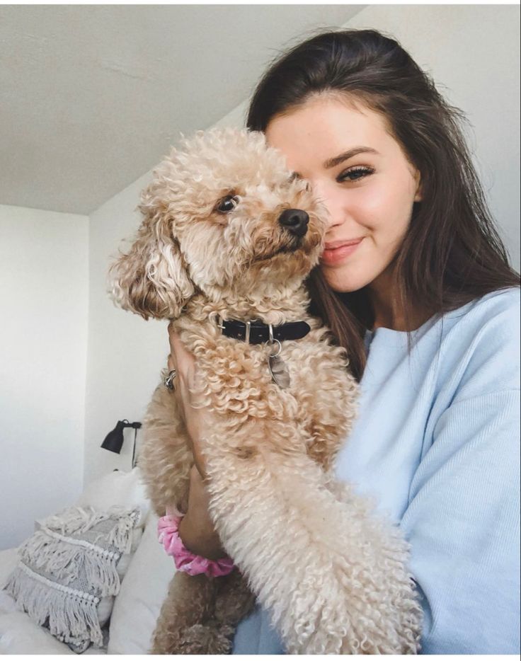 a woman holding a dog in her arms and smiling at the camera while sitting on a bed