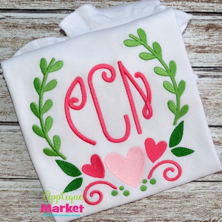 the embroidered monogrammed applique is on top of a white cloth with green leaves and hearts