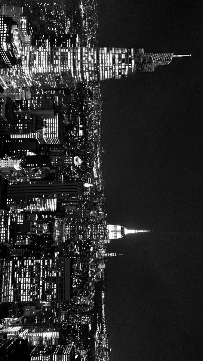 black and white photograph of the new york city skyline at night with skyscrapers lit up