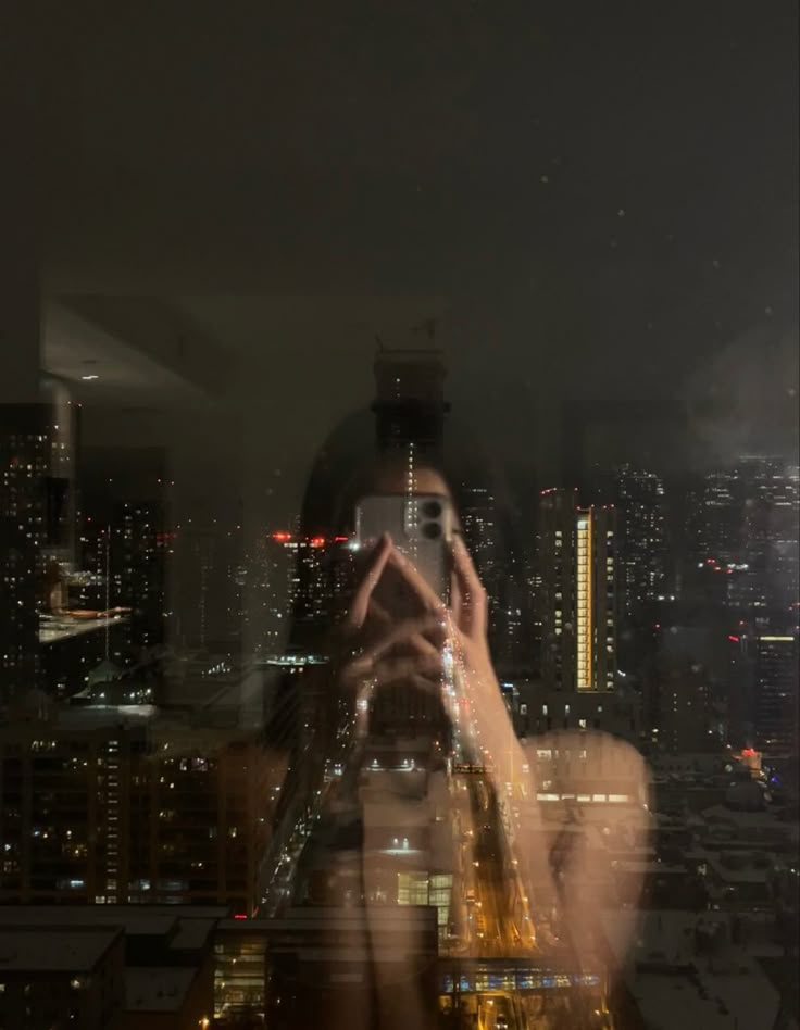 a woman taking a photo with her cell phone at night in front of a cityscape