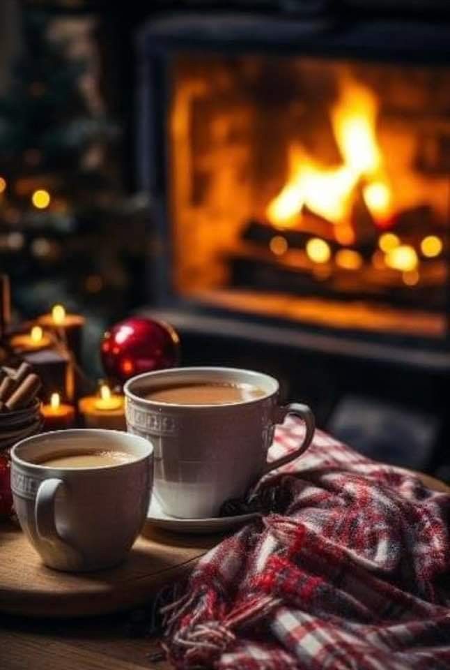 two cups of coffee sitting on a table in front of a fireplace with christmas decorations