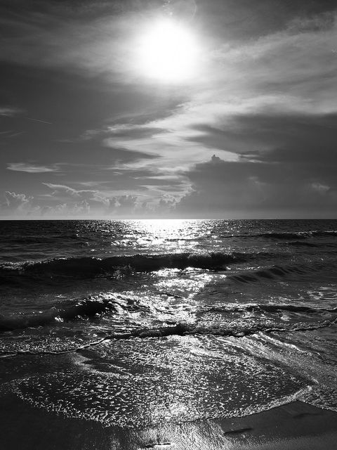 black and white photograph of the sun shining over the ocean