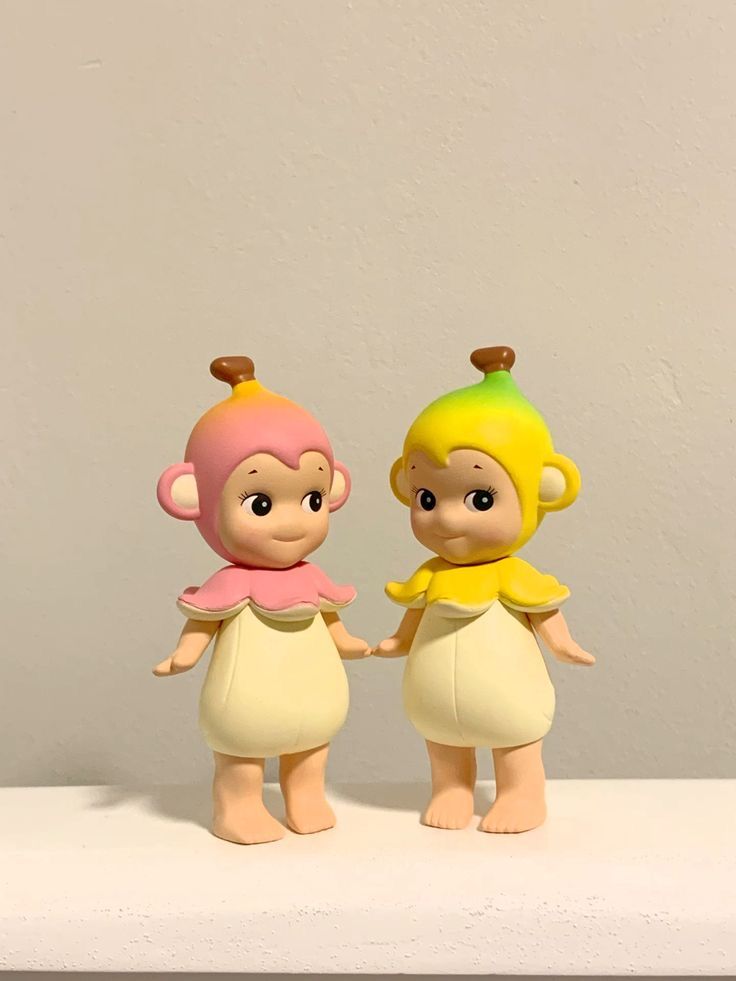 two little figurines standing on top of a white shelf next to each other