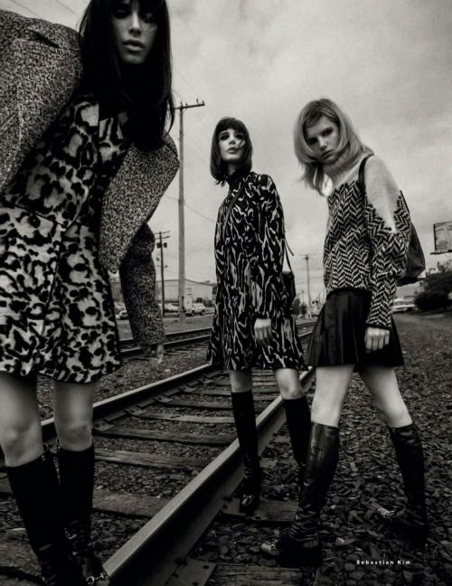 three women standing on train tracks with one holding an umbrella and the other wearing knee high boots