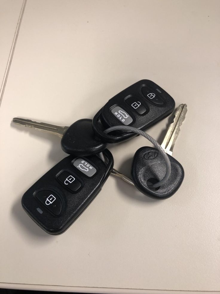 three car keys laying next to each other on top of a white table with two key fobs