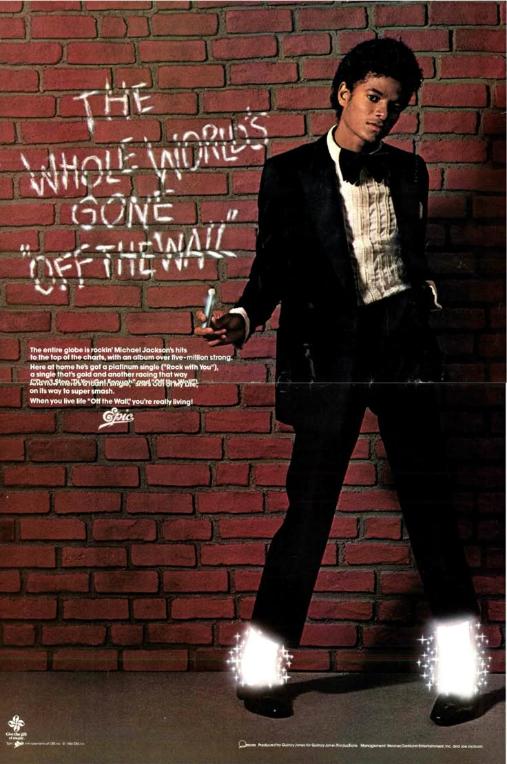 a man in a tuxedo leaning against a brick wall with words written on it