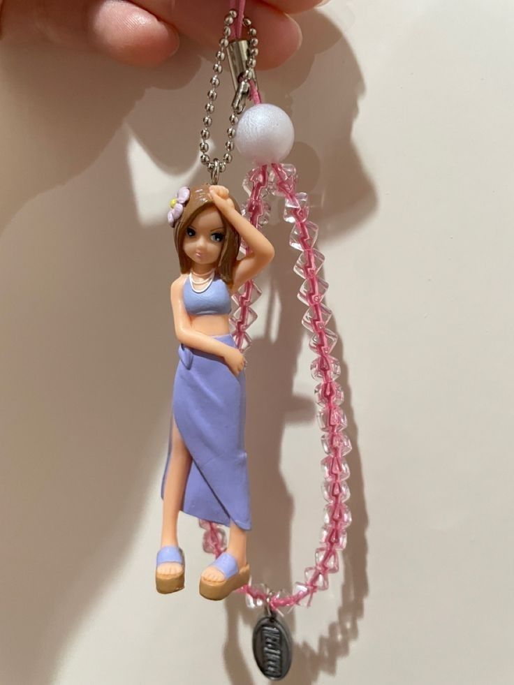 a key chain with a barbie doll hanging from it's side and a pink beaded necklace attached to it