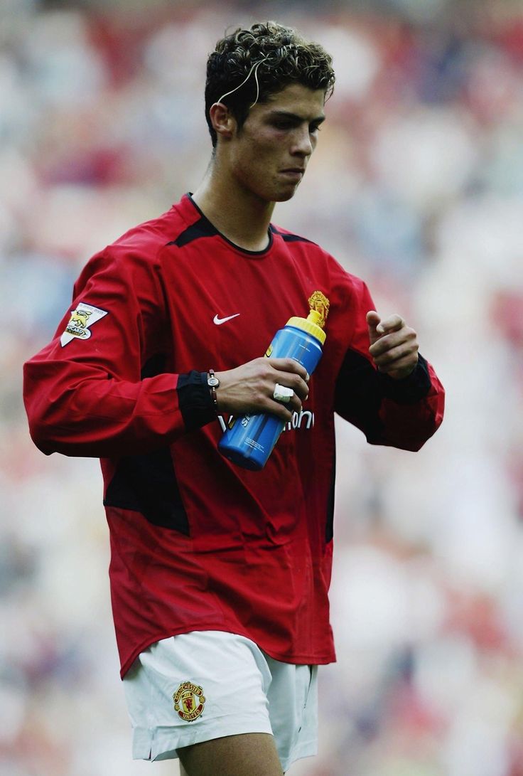 a young man holding a blue bottle in his right hand and standing on a soccer field