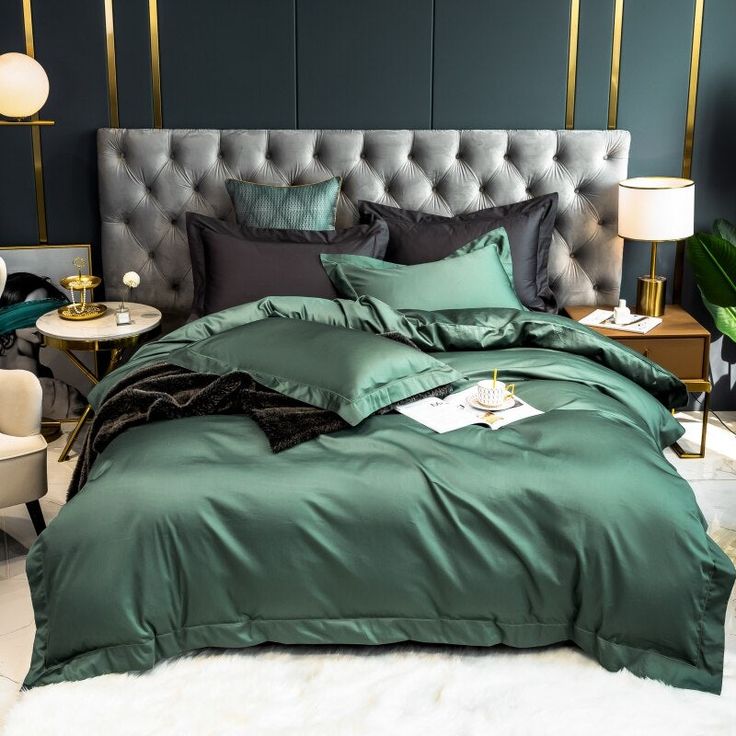 a bed with green comforter and pillows in a dark room next to a chair