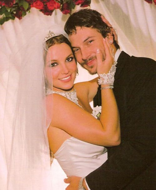 a bride and groom pose for a wedding photo in front of a white backdrop with red flowers