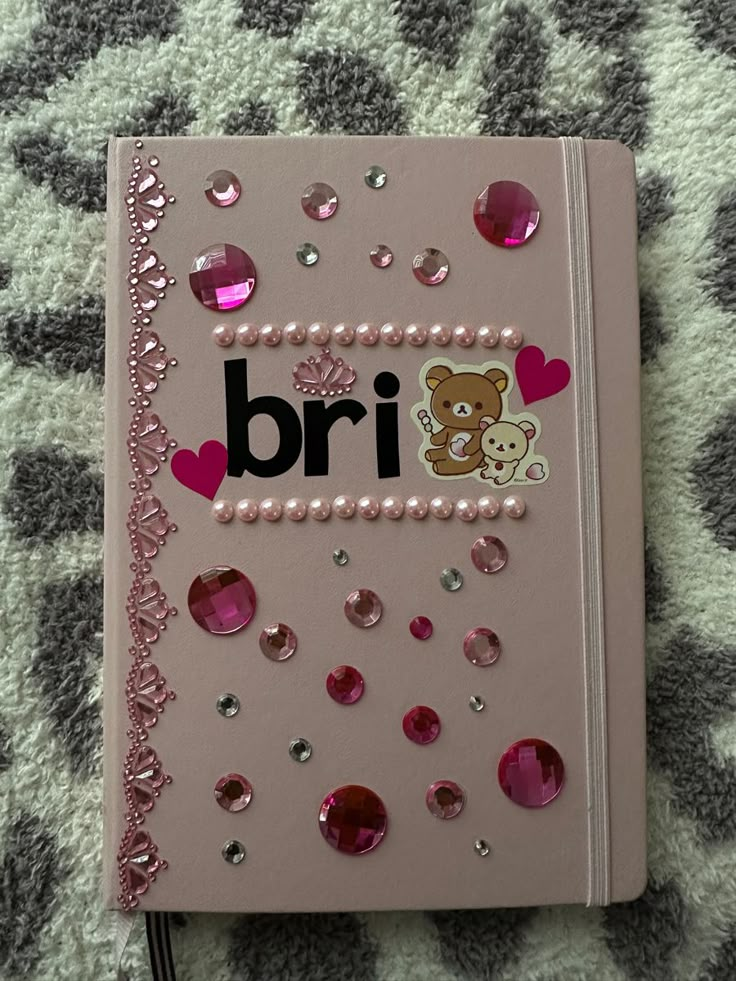 a pink notebook with the word bri written on it, surrounded by hearts and sequins