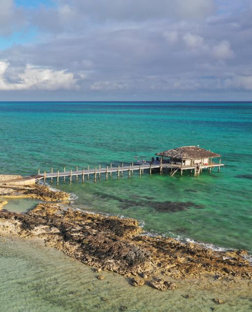 a house on a dock in the middle of the ocean with clear blue water around it