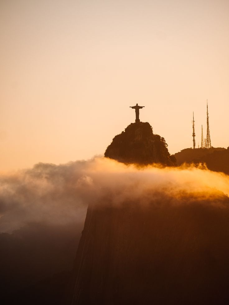 the statue of christ on top of a mountain with clouds in front of it at sunset