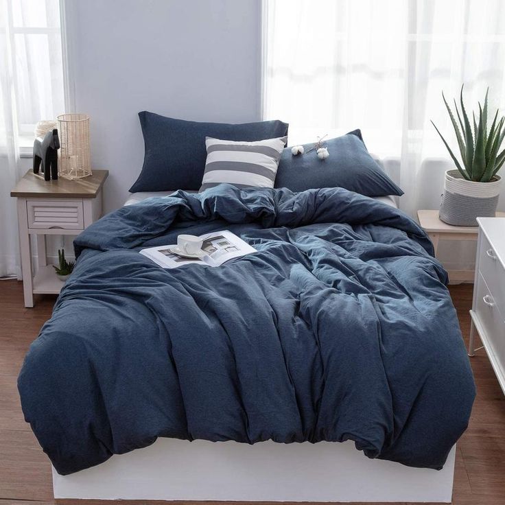 a bed with blue comforter and pillows in a room next to a window,