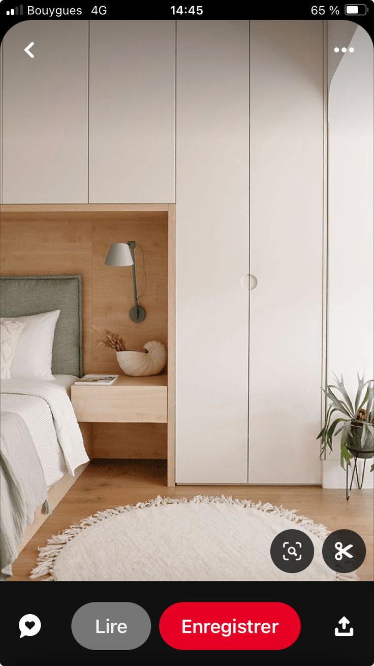 an iphone photo of a bedroom with white cupboards and a bed in the corner