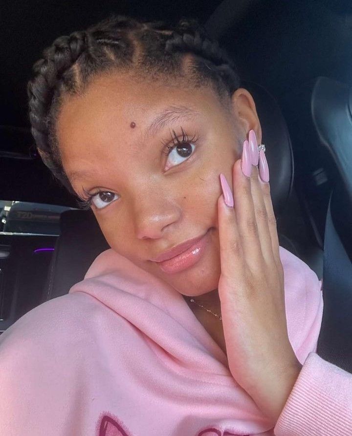 a young woman with braids in her hair wearing a pink sweatshirt and holding her hand up to her face