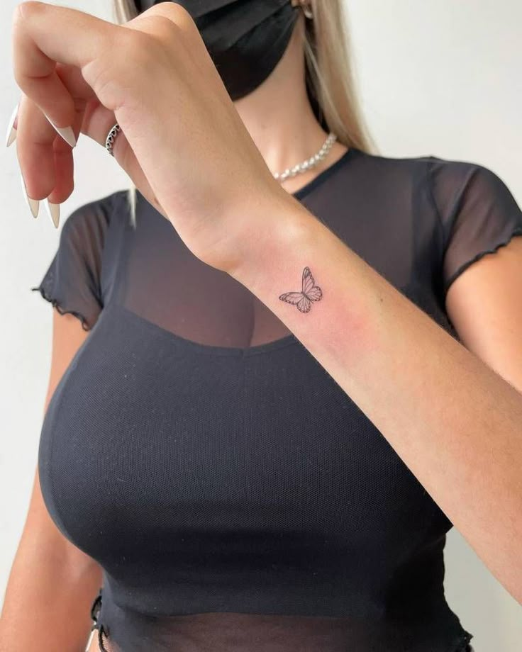 a woman with a butterfly tattoo on her left arm, wearing a black shirt and mask