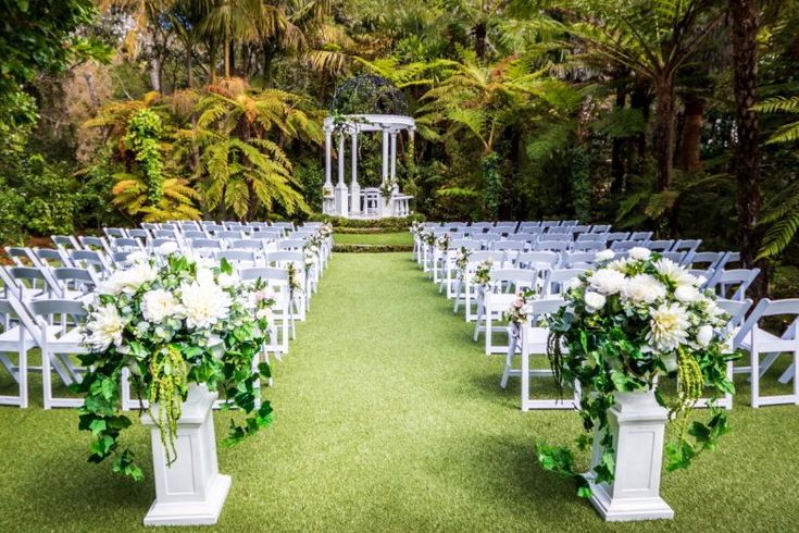 an outdoor ceremony set up with white chairs and green floral centerpieces on the grass