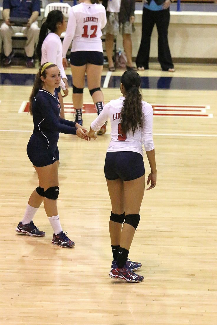 two female volleyball players shake hands on the court as people watch from the sidelines