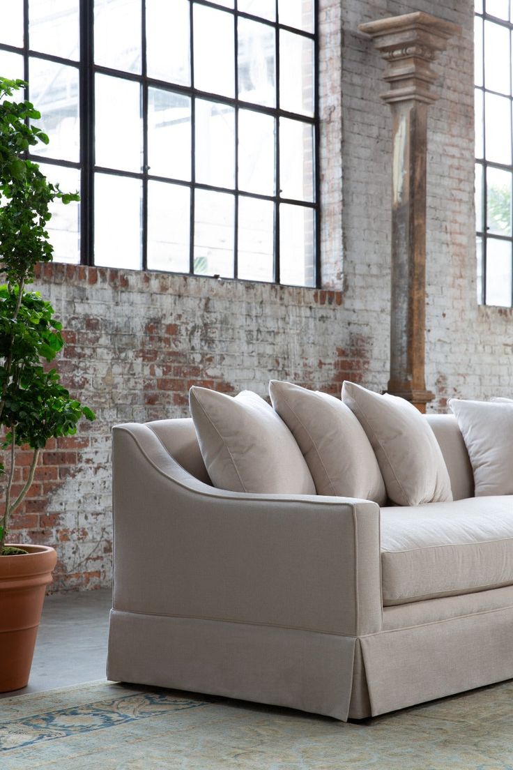 a couch with pillows on it in front of a brick wall and potted plant