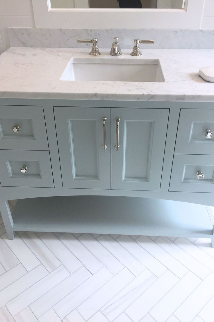 a bathroom vanity with two sinks and a mirror in the backround, along with herringbone tile flooring