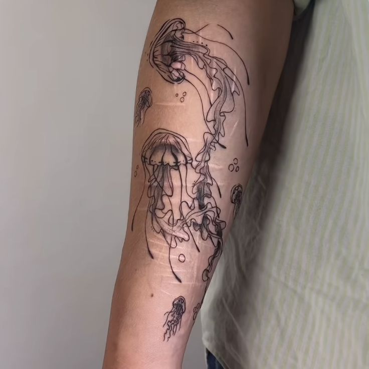 a man's arm with an octopus tattoo on it and jellyfish in the water