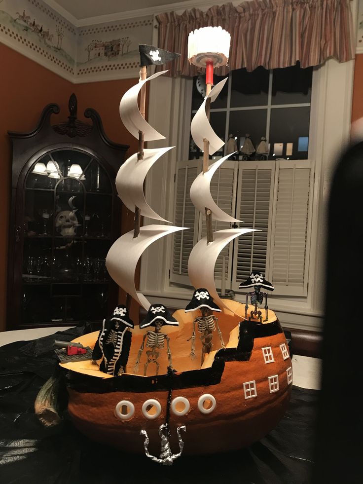 a wooden pirate ship with white sails on a table in front of a bay window