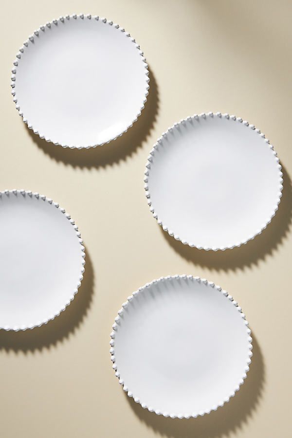 four white plates with scalloped edges are arranged on a beige surface, one is empty