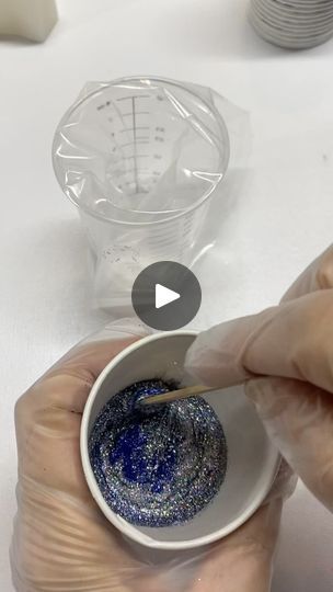 a person holding a small bowl with blue liquid in it and another hand reaching out to the bowl