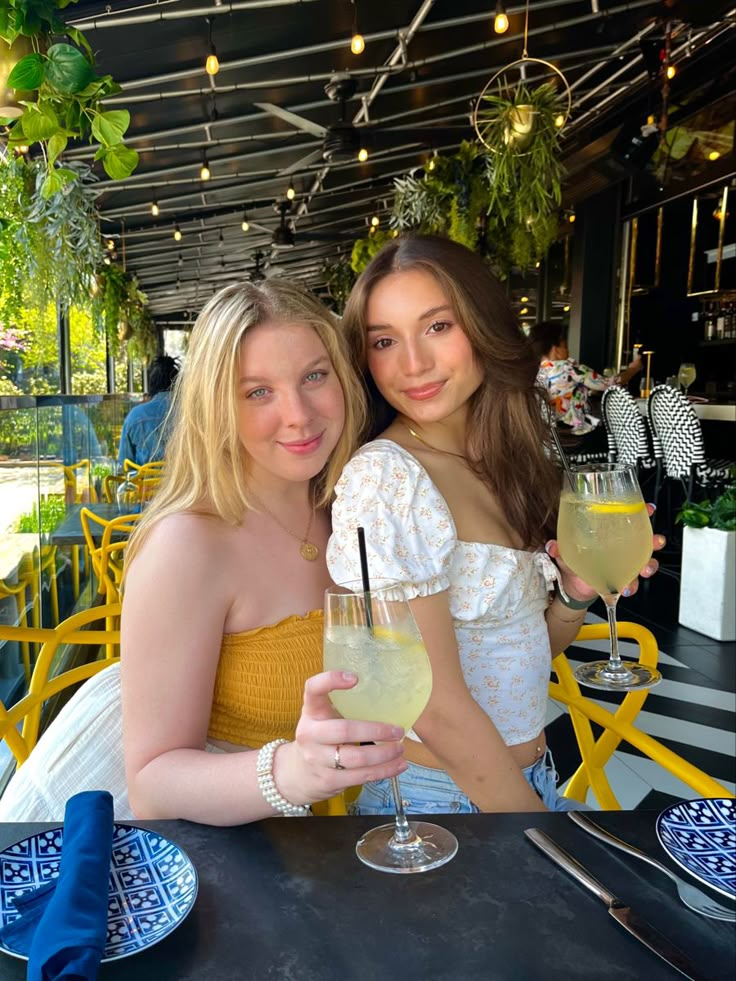 two young women sitting at a table with drinks in front of them, posing for the camera