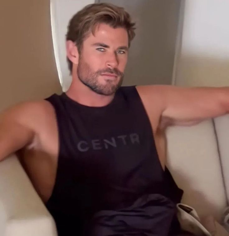 a man sitting on top of a white couch wearing a tank top and black shorts