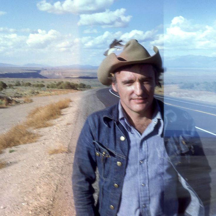 a man wearing a cowboy hat standing next to a road